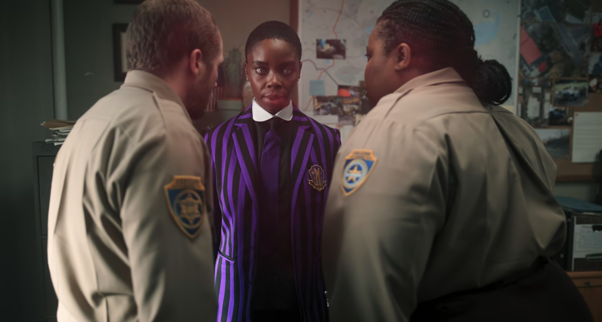 Bianca Barclay standing confidently between a town deputy and Sheriff Santiago. She wears a Nevermore Academy uniform with a purple and black striped blazer, staring directly ahead with an intense expression.