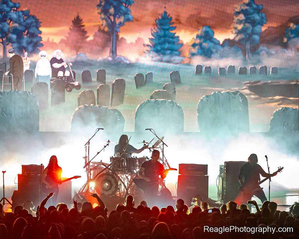 Dethklok with an animation with gravestones on the screen behind the band