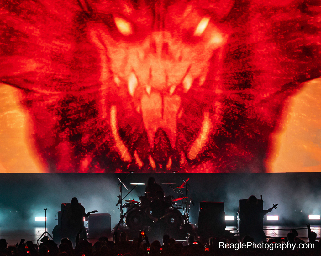 Dethklok appearing as a silhouette with a large fiery screen above them