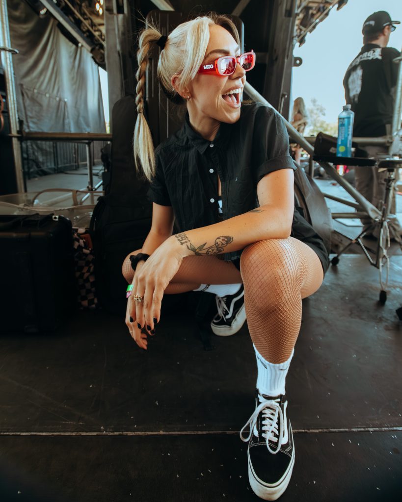 MEGG backstage at Vans Warped Tour wearing red logo sunglasses and Vans, celebrating “IDC” single release.