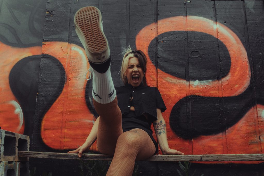 Alternative punk artist MEGG kicking toward the camera in front of graffiti wall