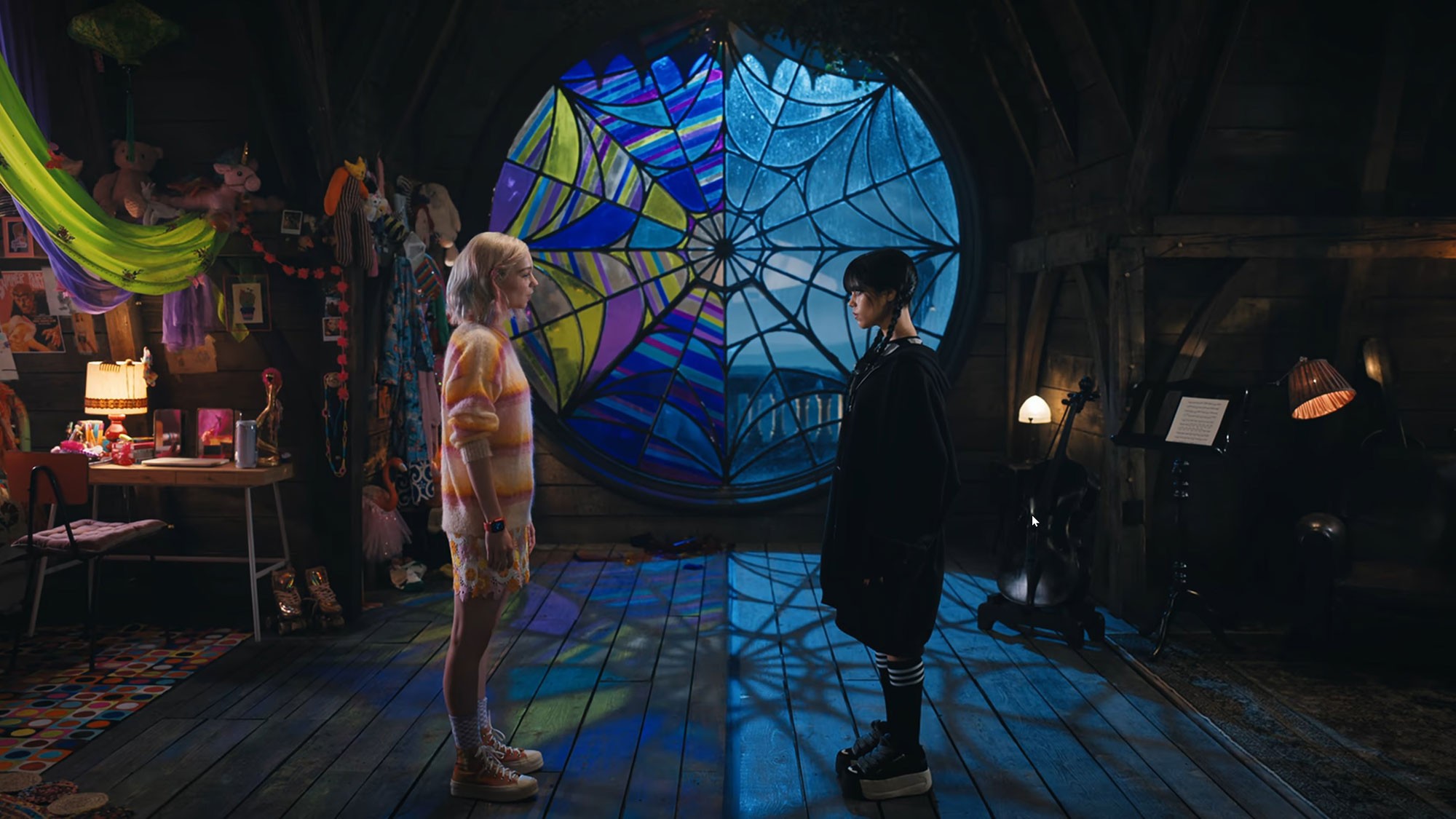 Enid Sinclair and Wednesday Addams standing face-to-face in front of the stained-glass spiderweb window in Netflix’s "Wednesday."