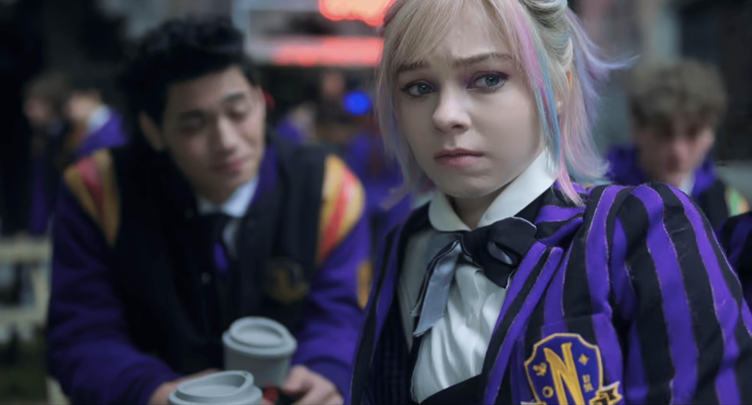 Bruno sits with Enid Sinclair at a Nevermore schoolyard table; the lens shifts from him to her as she gazes anxiously at Wednesday and Agnes across the yard.