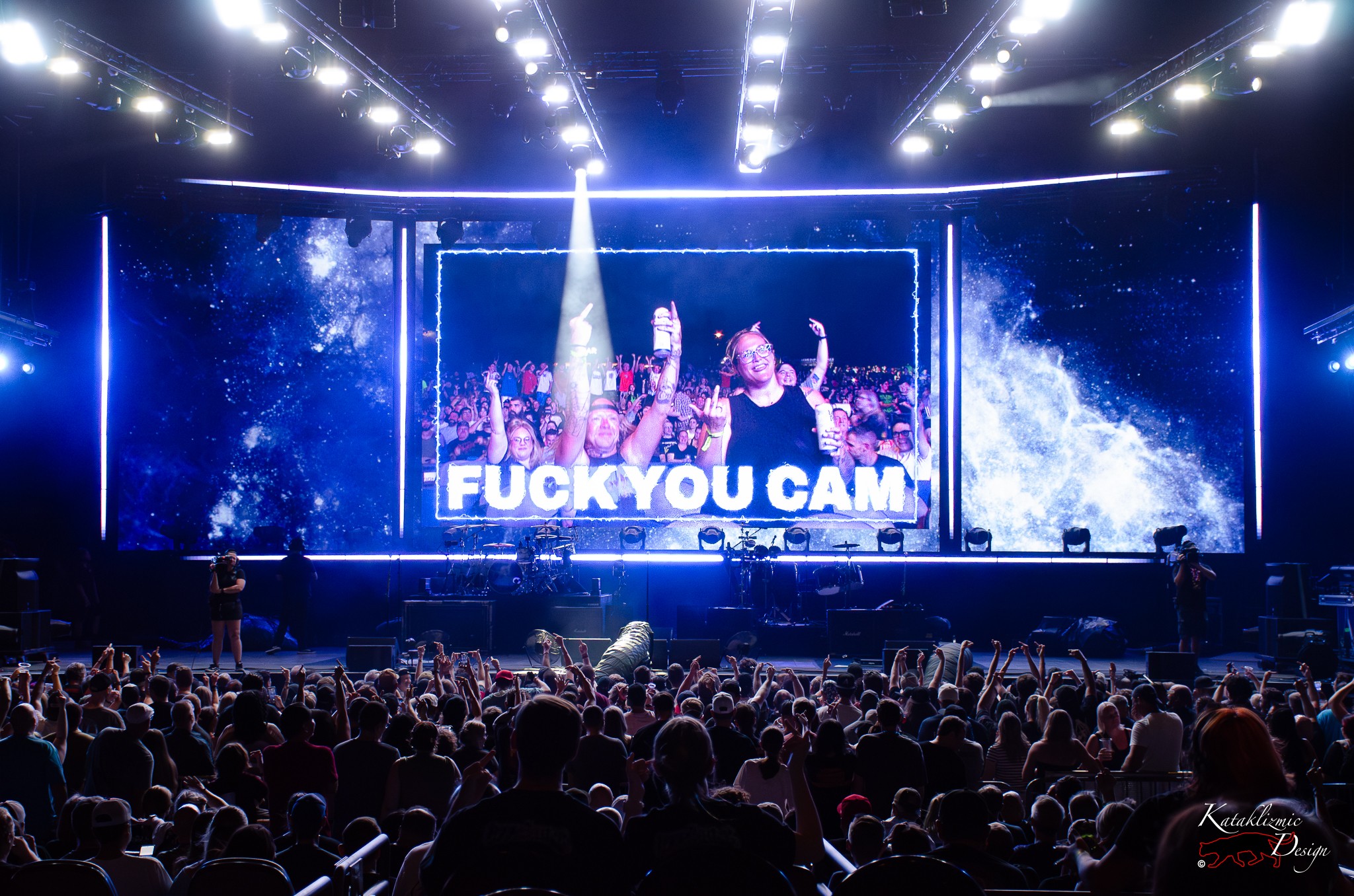 Crowd at The Offspring concert reacting to the giant screen displaying the “Fuck You Cam,” with fans flipping off the camera in good fun.