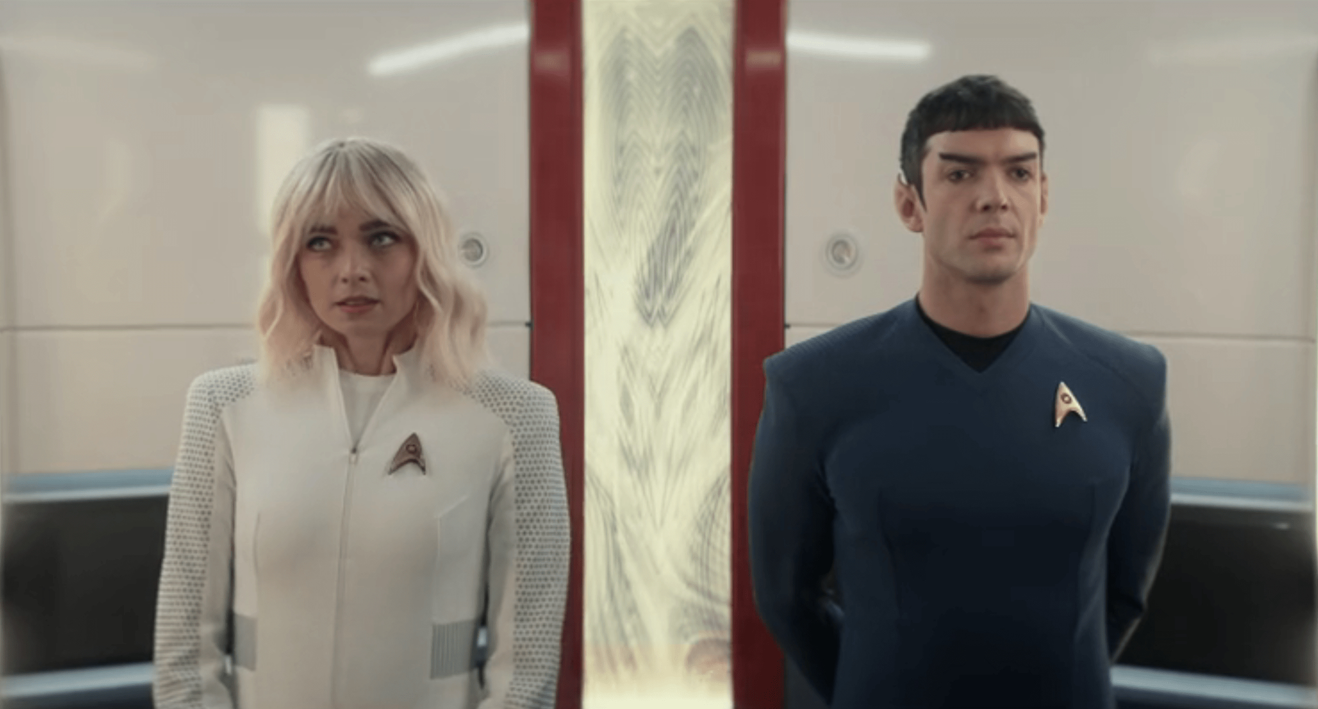 Spock and Chapel stand silently beside each other, framed symmetrically with a glowing red-and-gold panel between them, their body language highlighting emotional distance.