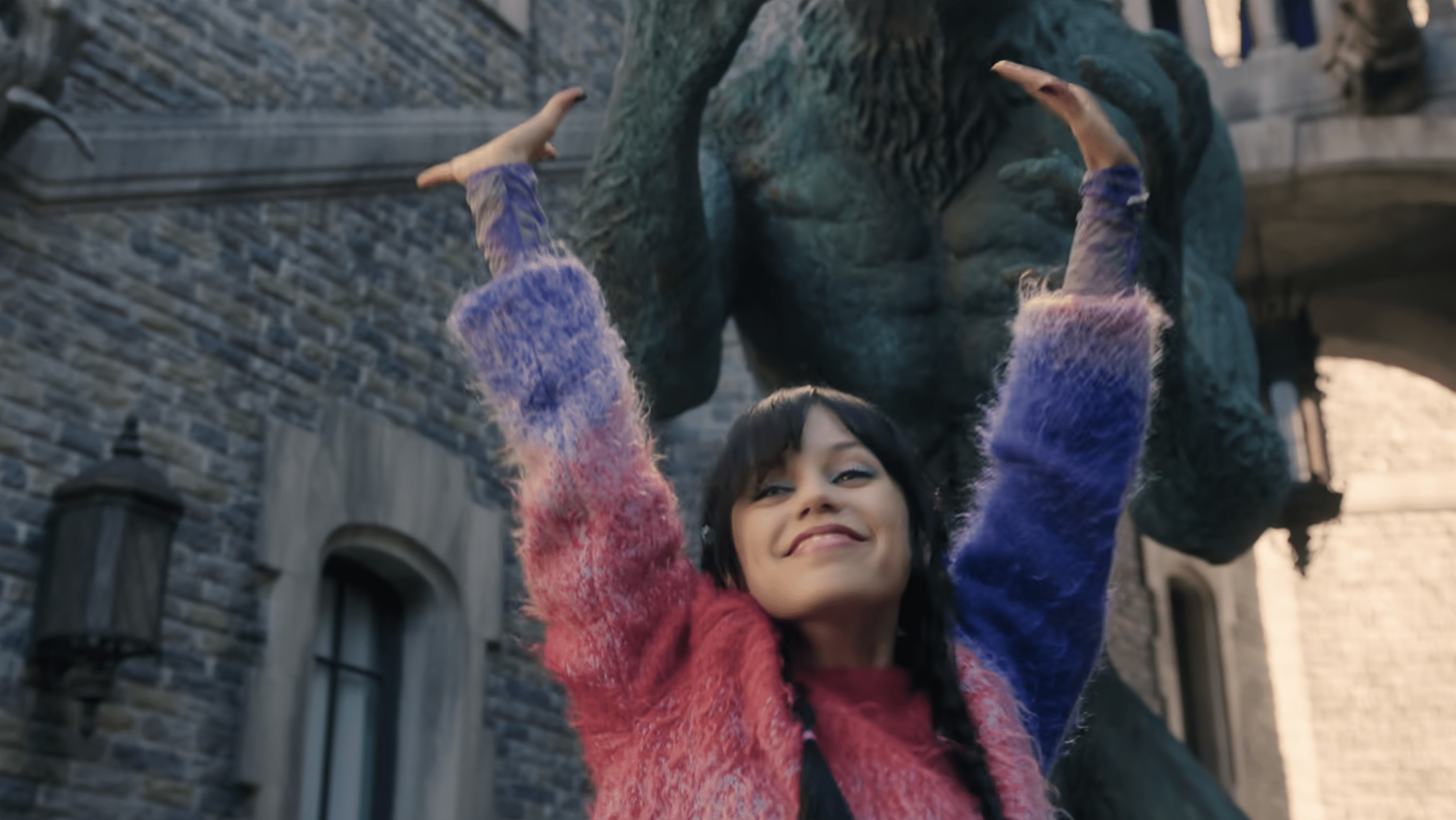 Enid, inhabiting Wednesday’s body, dances in a vibrant pink-and-purple sweater in the Nevermore courtyard.