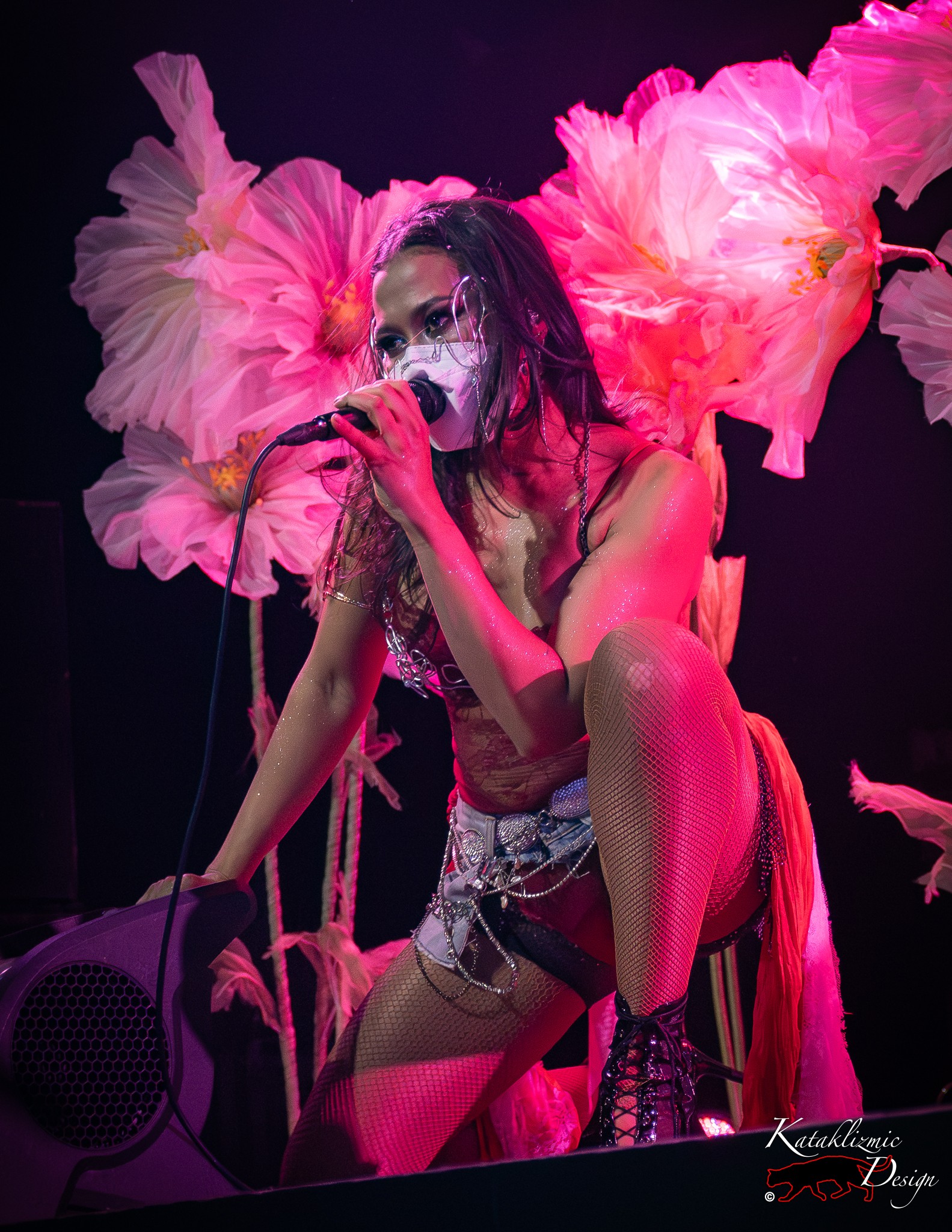 Singer kneels at the edge of the stage, singing into a microphone in front of towering pink paper flowers during yuniVERSE's set at The Van Buren in Phoenix, Arizona.