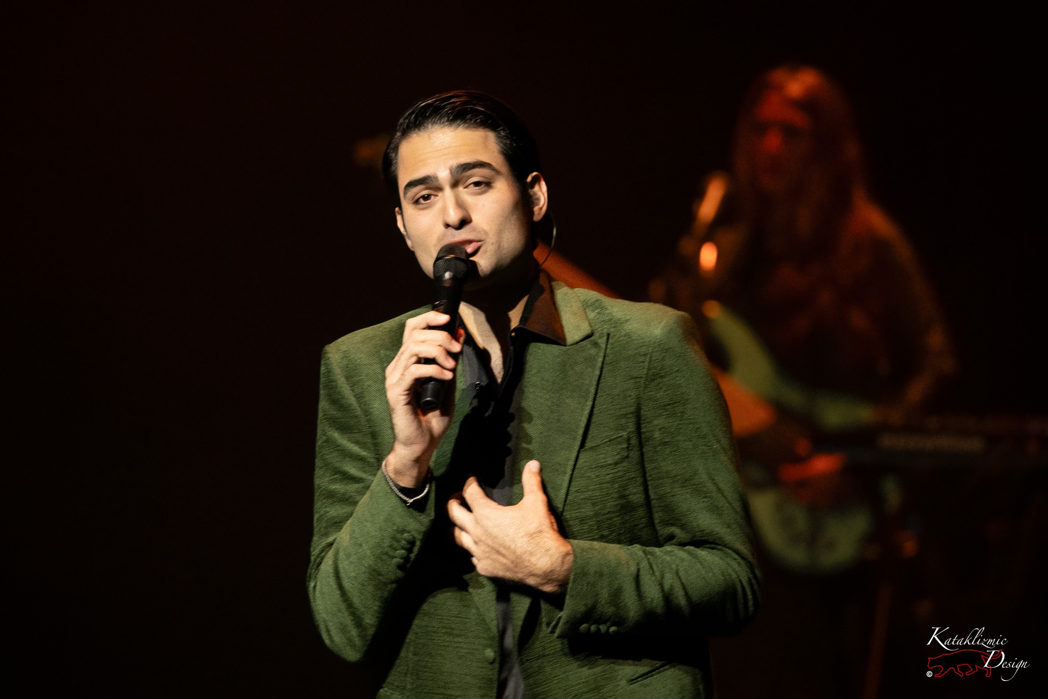 Matteo Bocelli singing into a microphone with his hand over his heart in warm stage lighting.