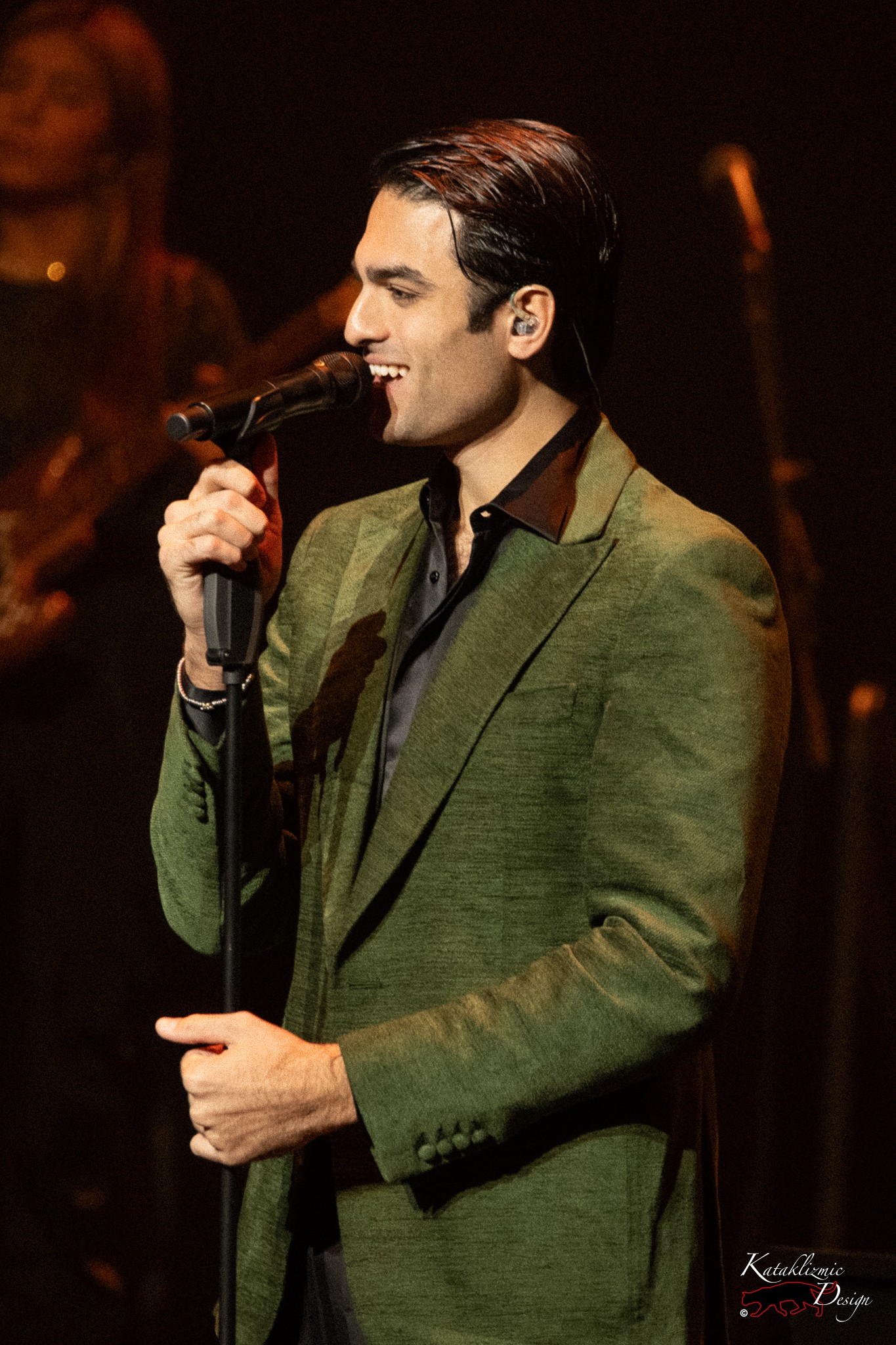 Matteo Bocelli smiling at the microphone in a green jacket during his live performance.
