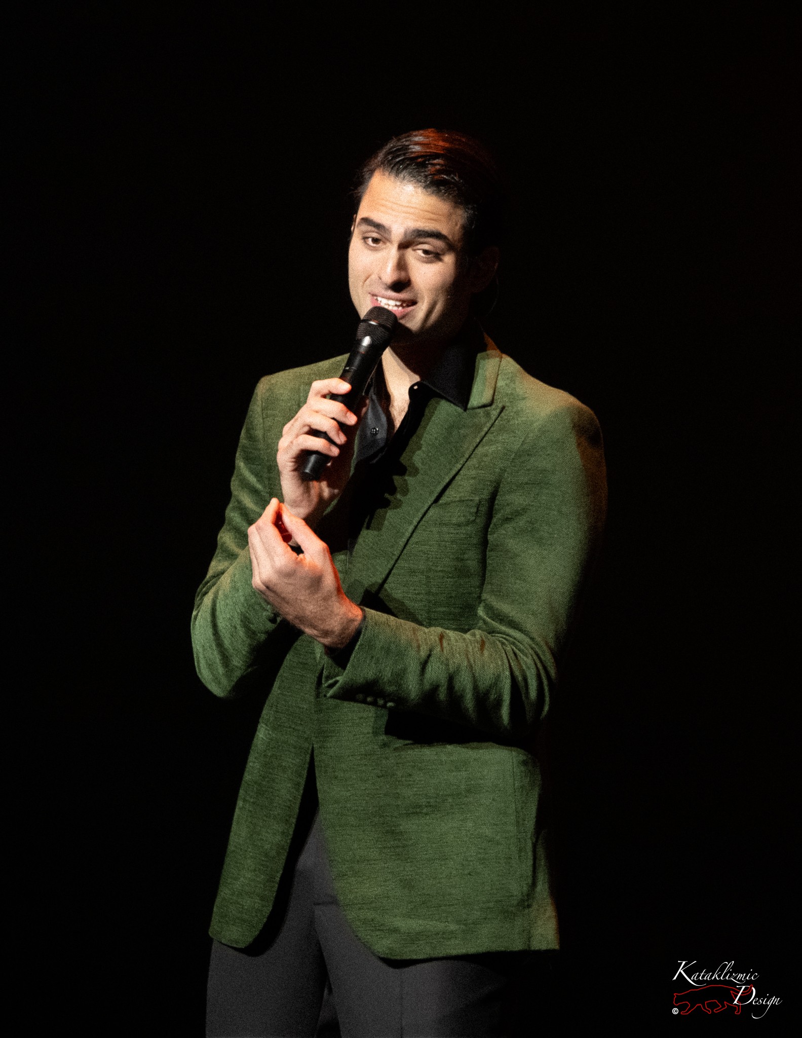 Matteo Bocelli singing into a handheld microphone in a green blazer under spotlight at Mesa Arts Center.