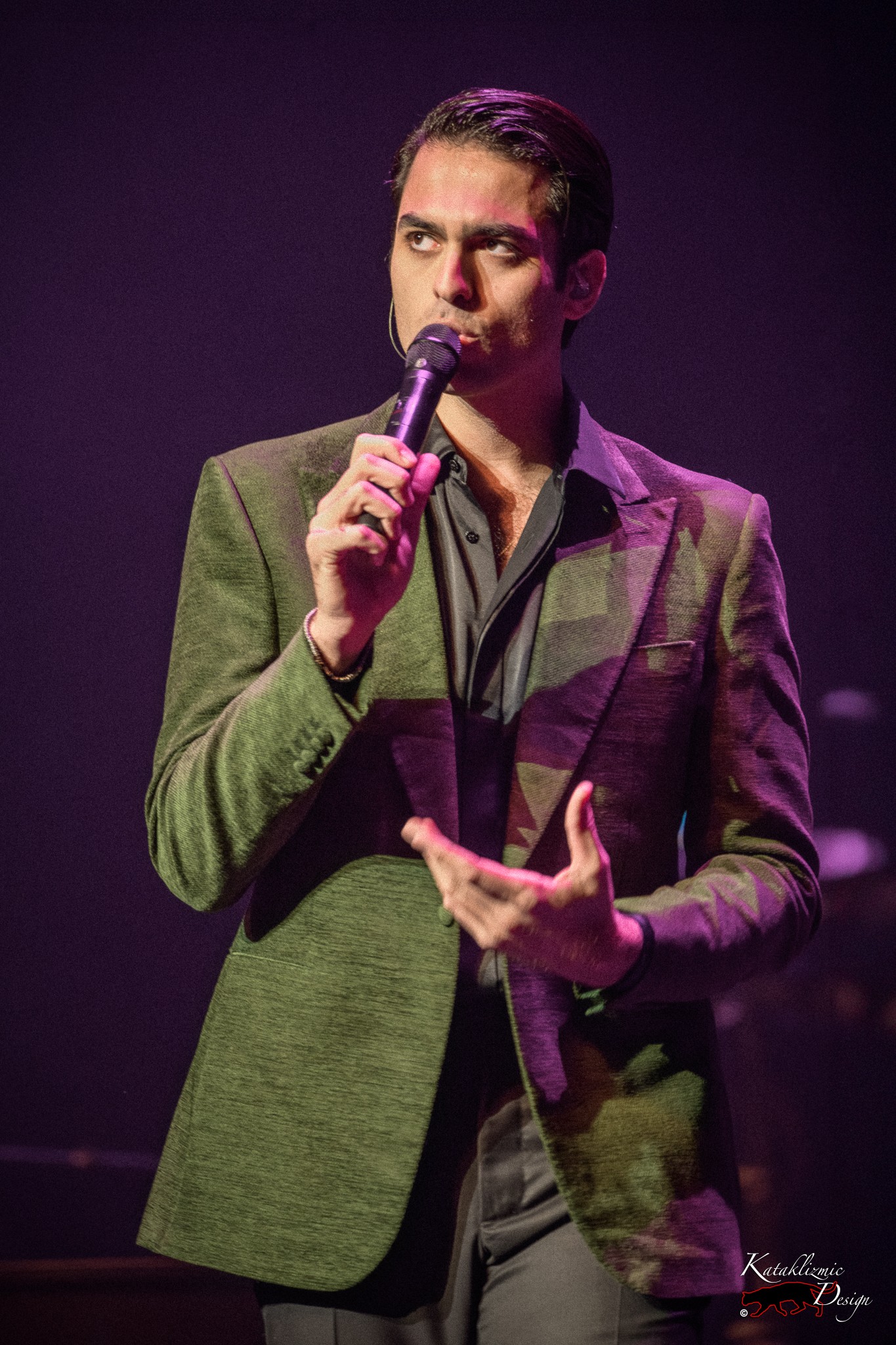 Matteo Bocelli singing into a handheld microphone in a green blazer, lit by purple stage lighting.