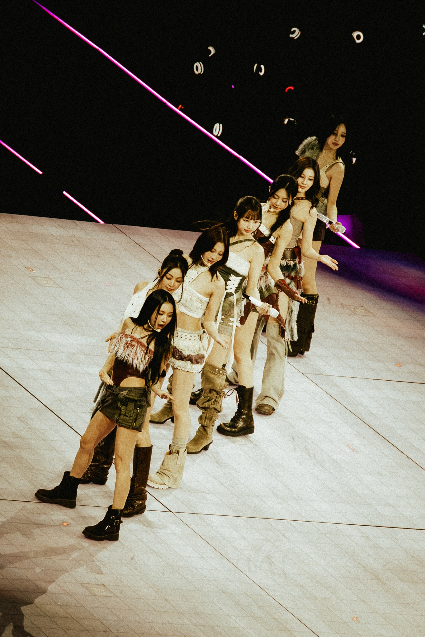 TWICE performs in a diagonal line formation, wearing coordinated earthy-toned outfits as they move in sync across the stage.