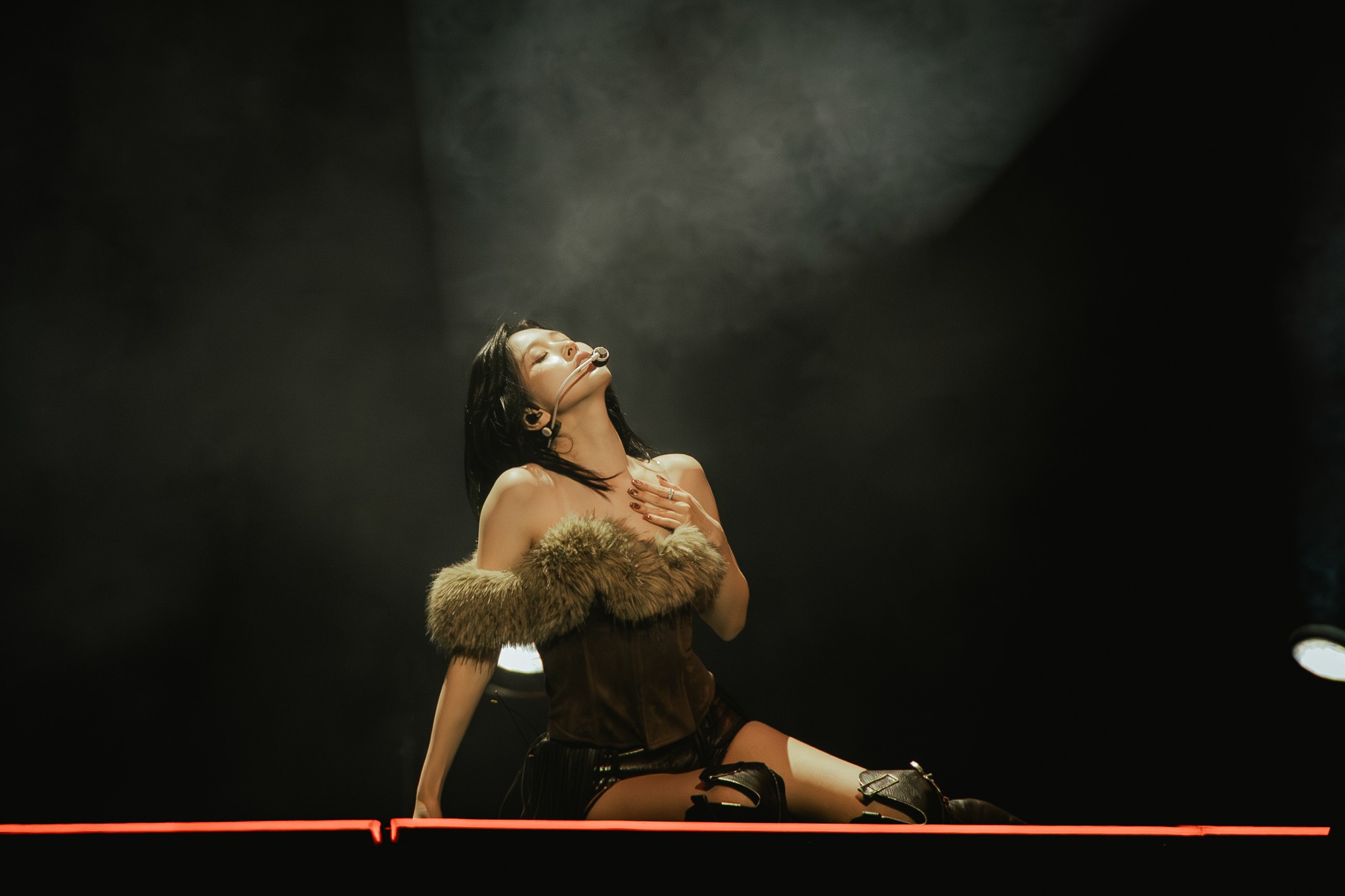 Mina of TWICE reclines on one hip in a dramatic stage pose, illuminated by a single spotlight as light haze surrounds her.