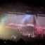Wide crowd shot inside an arena during a Nine Inch Nails concert, with the NIN logo projected on large side screens, bright stage lighting cutting through haze, and a packed floor and seating bowl.