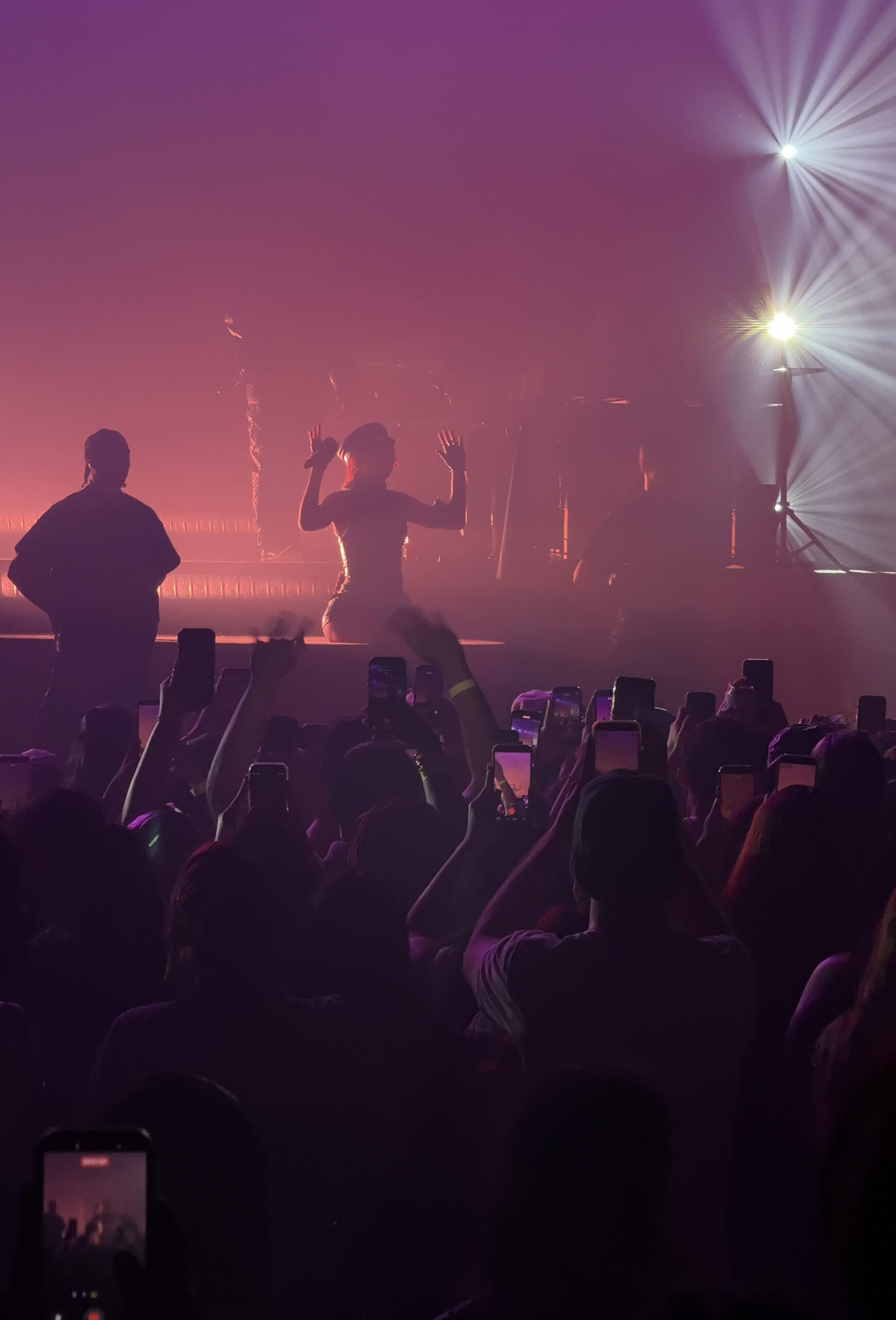Mariah the Scientist lifts her hands toward the crowd through pink-purple haze as fans raise phones and respond from the floor.