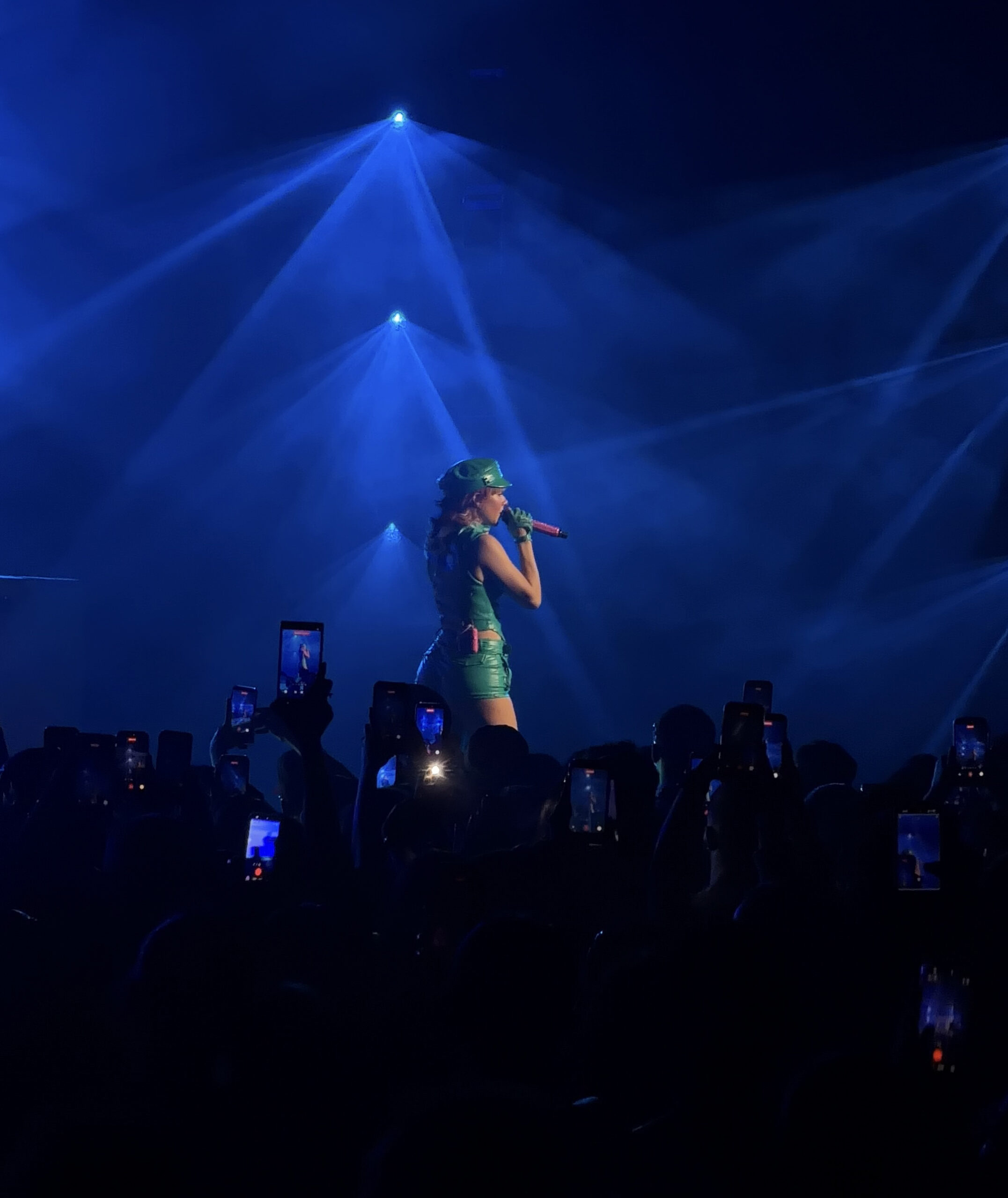 Mariah the Scientist performs under deep blue stage lighting as the crowd watches and records on phones.