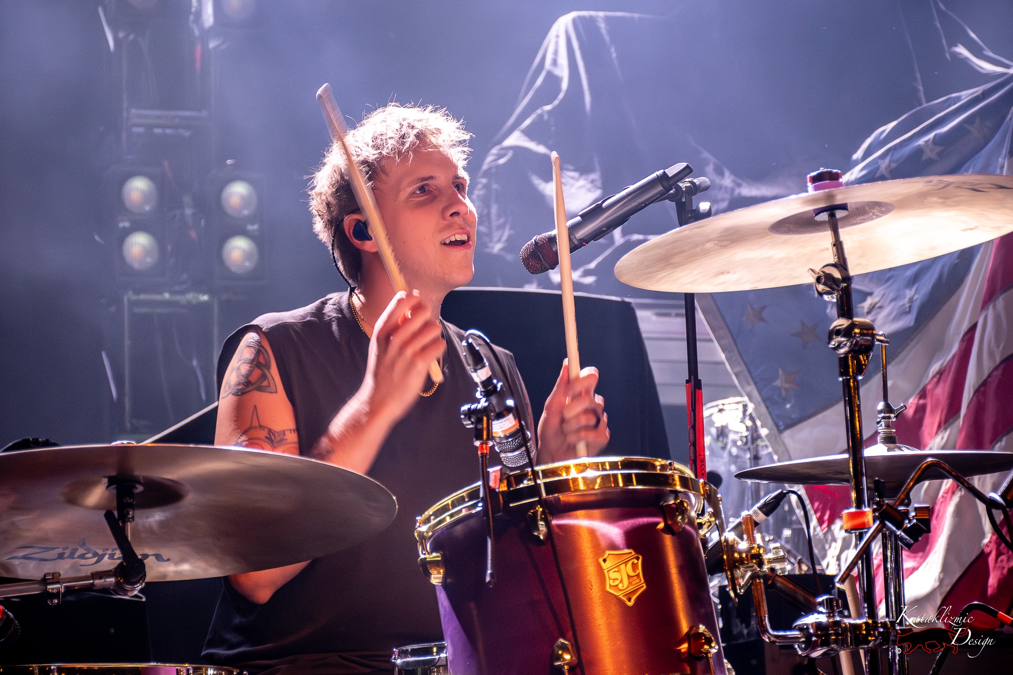 Arrows in Action drummer Jesse Frimmel smiles behind the drum kit with drumsticks raised during a live performance.