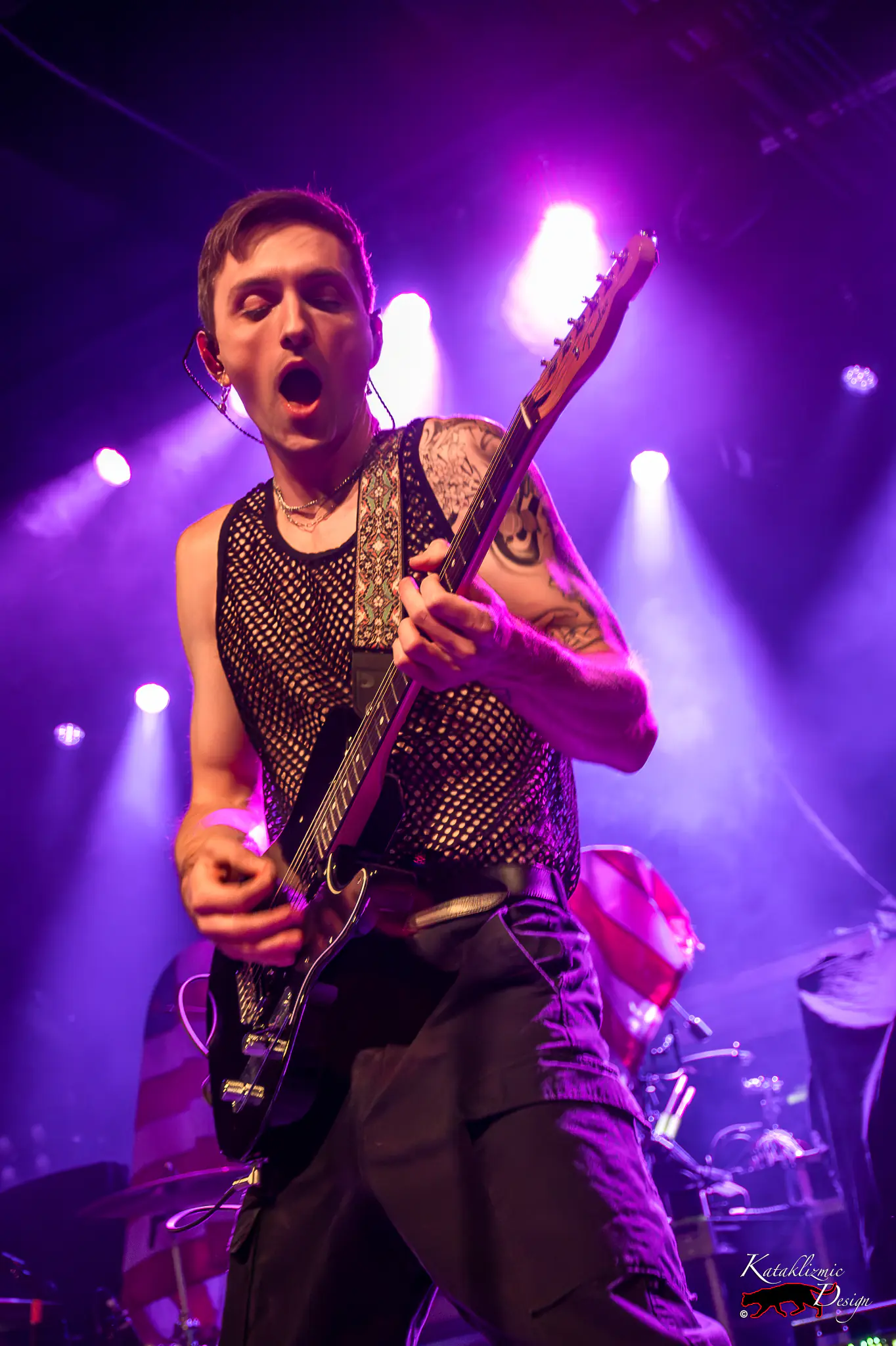 Arrows in Action guitarist Matt Fowler performs near the front of the stage under vivid purple lighting.