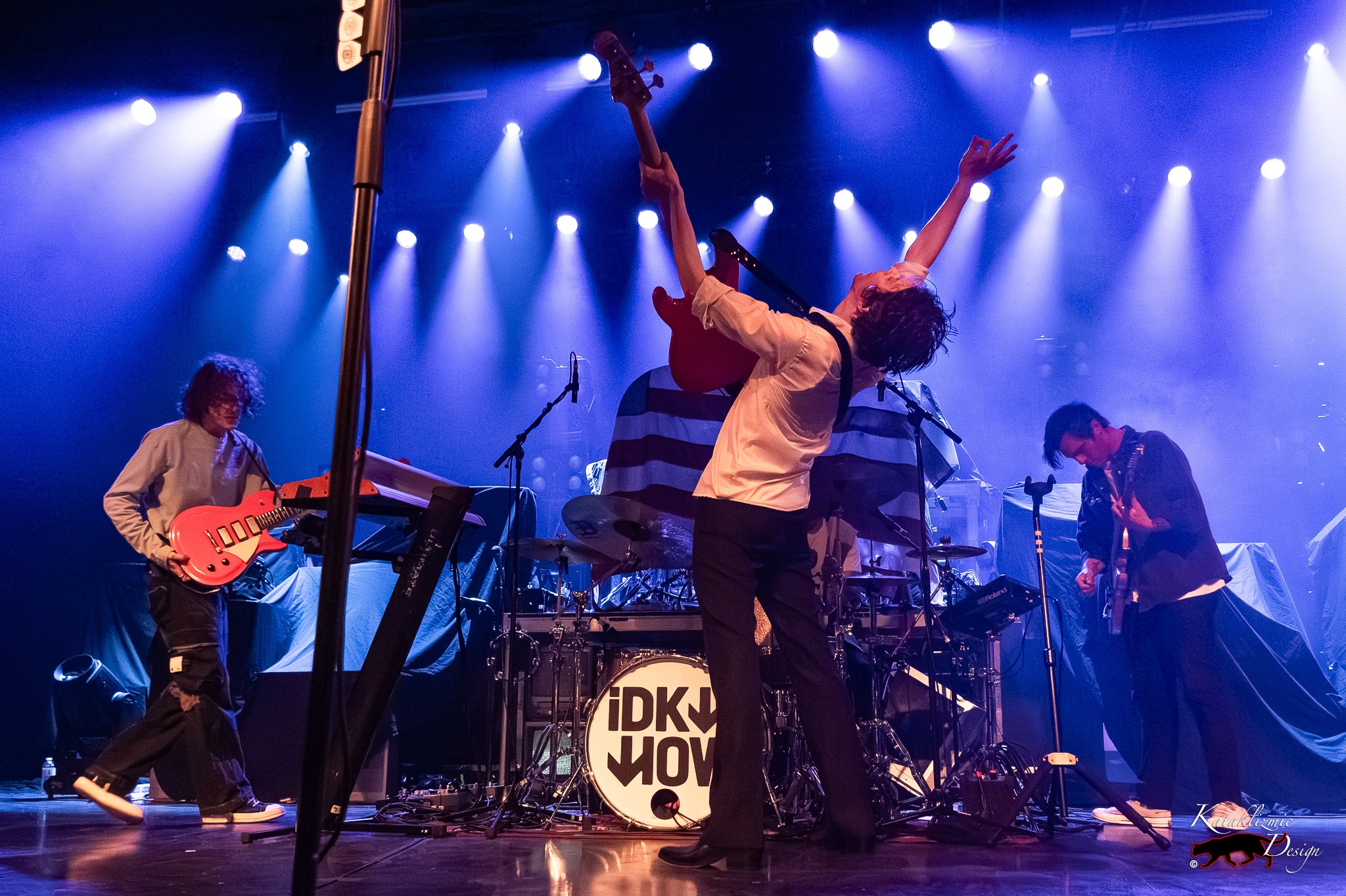 iDKHOW performs onstage as Dallon Weekes leans back with his guitar under blue concert lights.