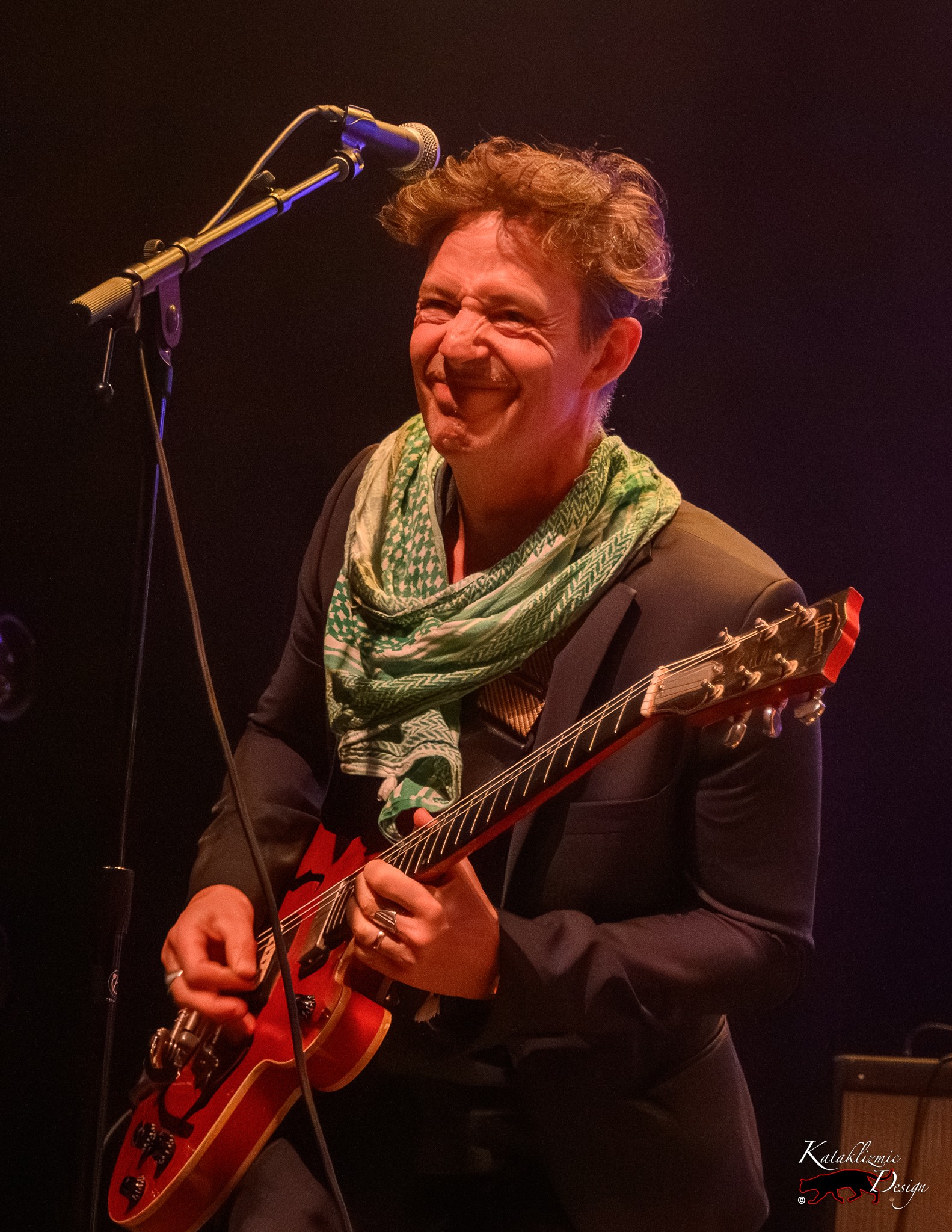 Andrew Whiteman of Broken Social Scene smiles while playing guitar onstage.