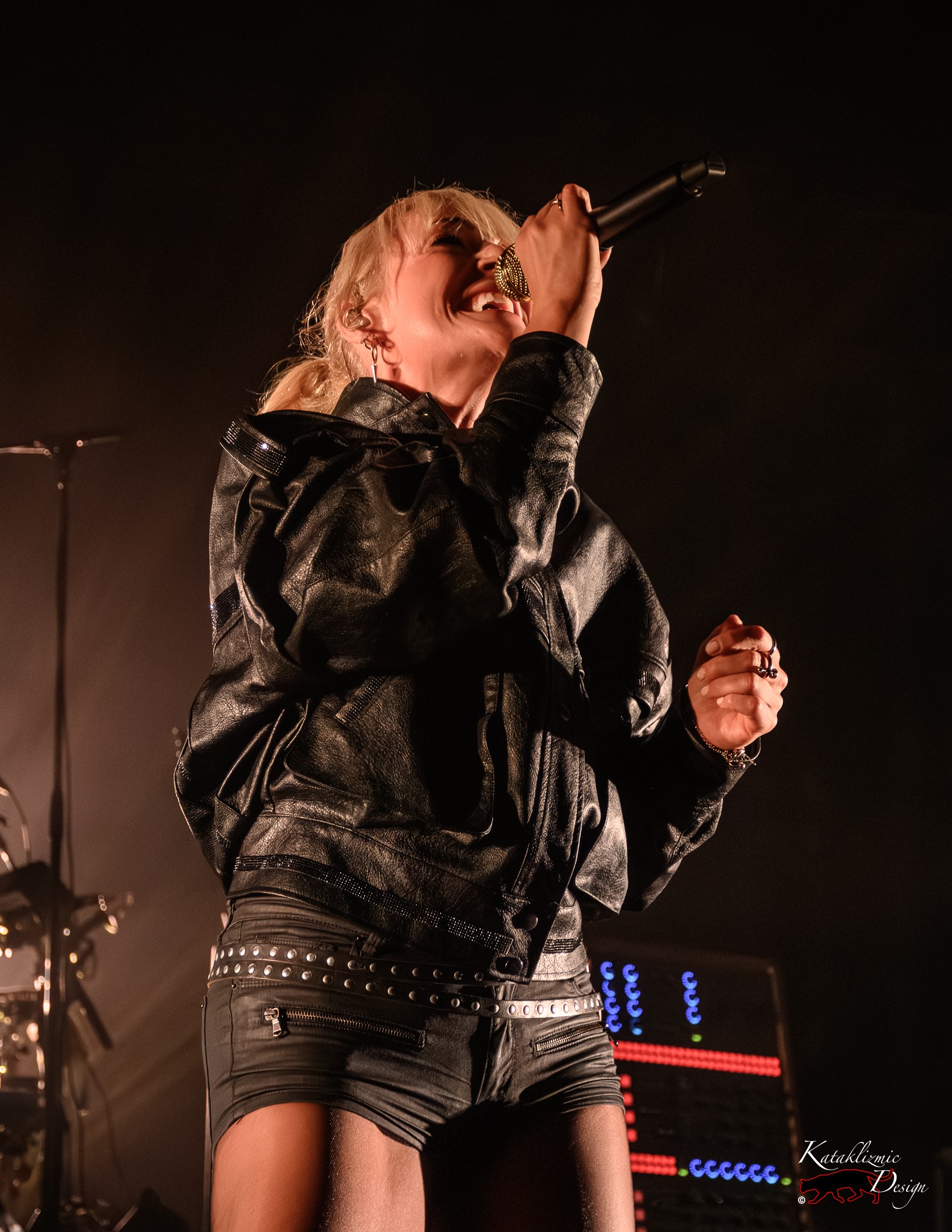 Emily Haines of Metric sings into a gold microphone under warm stage lighting.