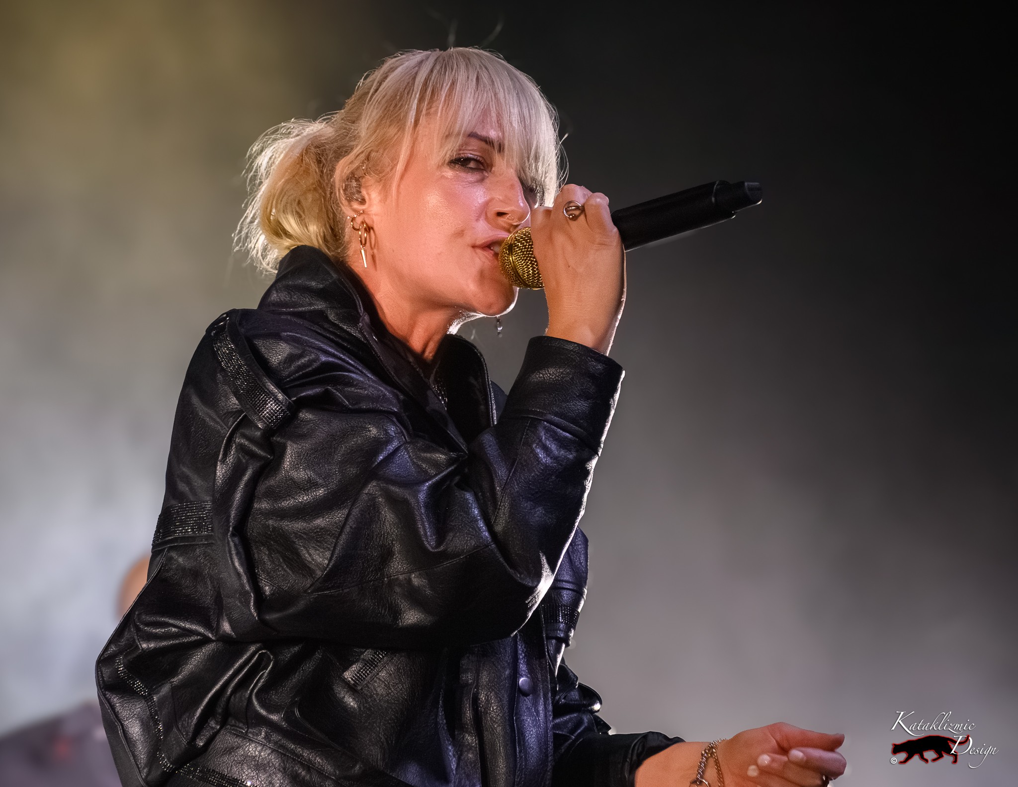 Emily Haines of Metric sings into a gold microphone while wearing a black leather jacket onstage.