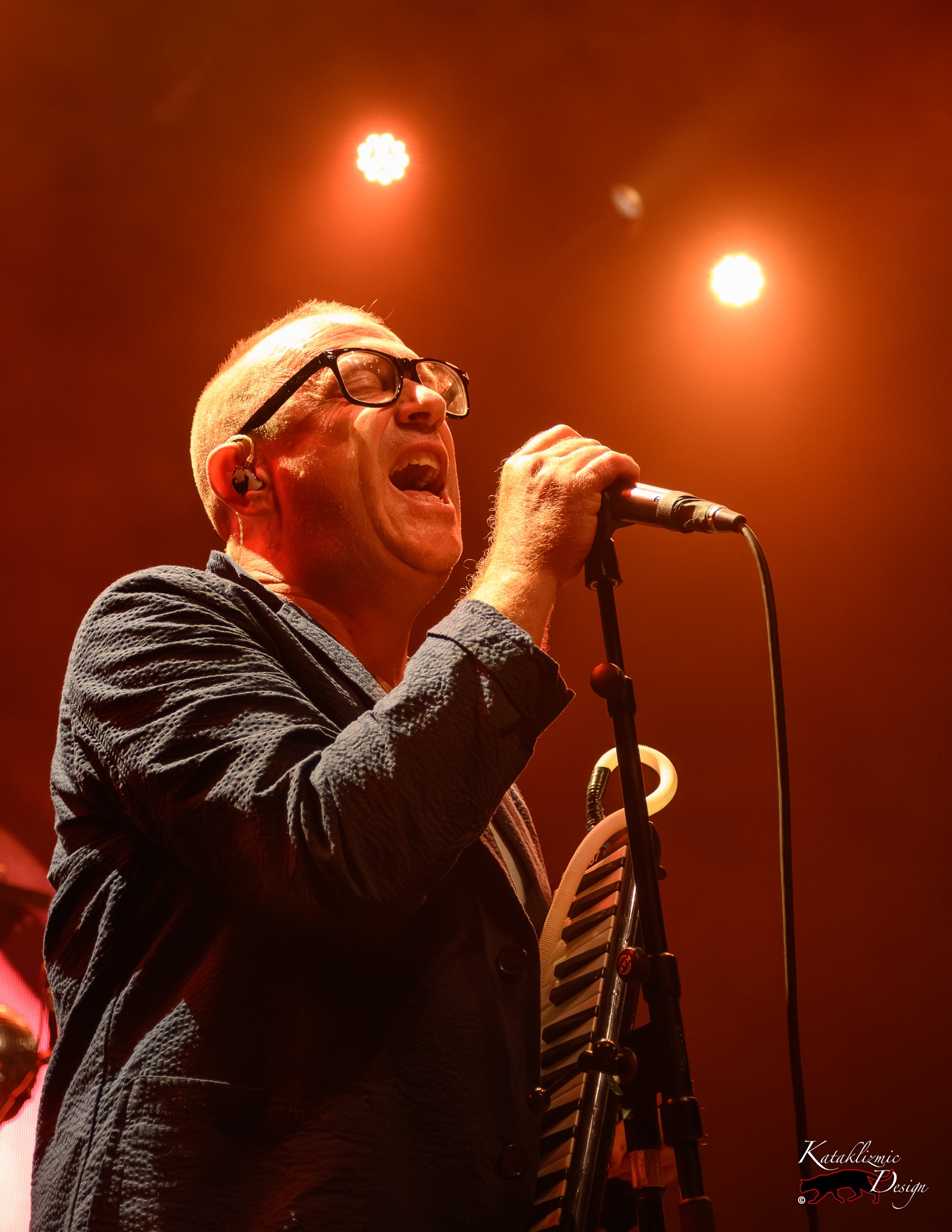 Torquil Campbell of Stars sings into a microphone under warm orange stage lights during the All The Feelings Tour.