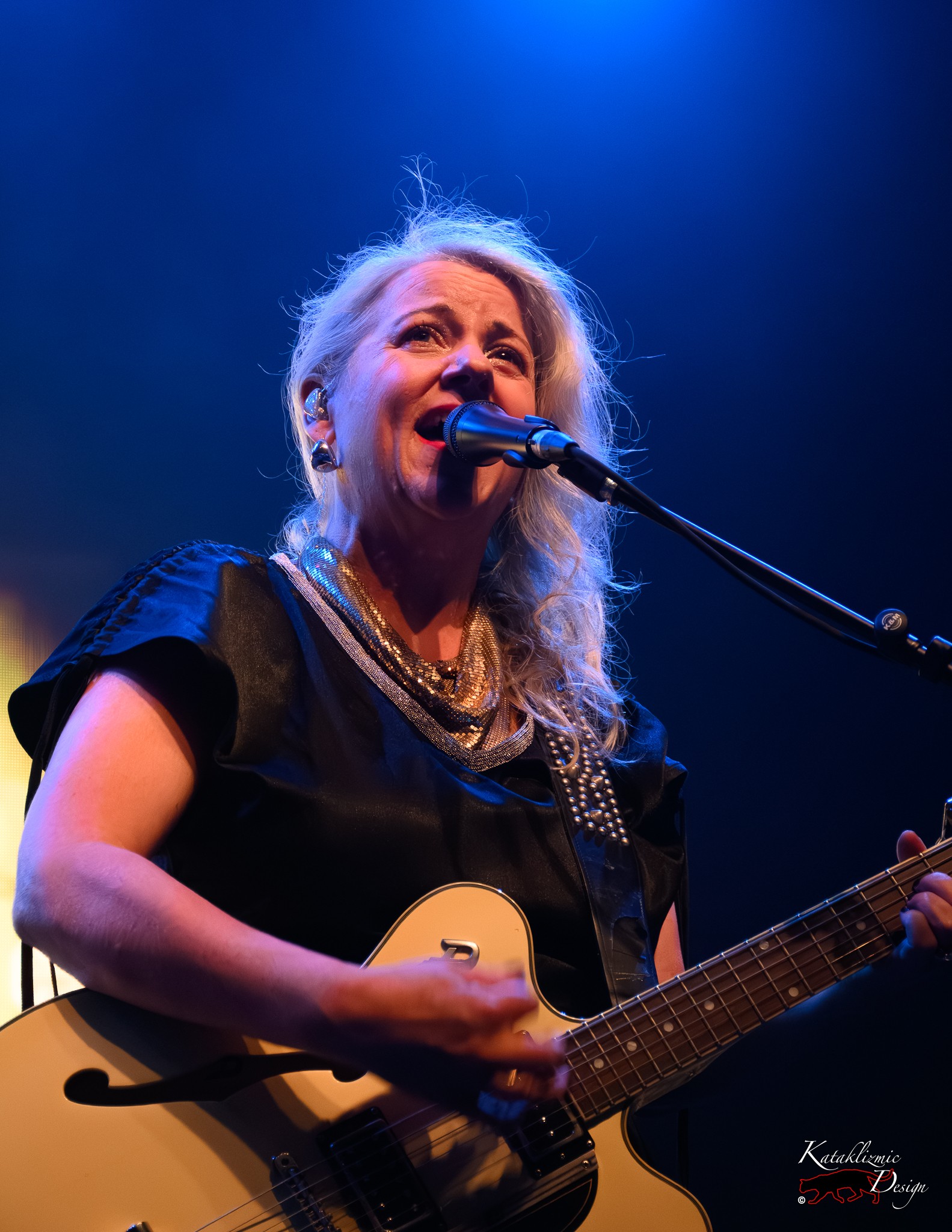 Amy Millan of Stars sings and plays guitar onstage under blue lighting.