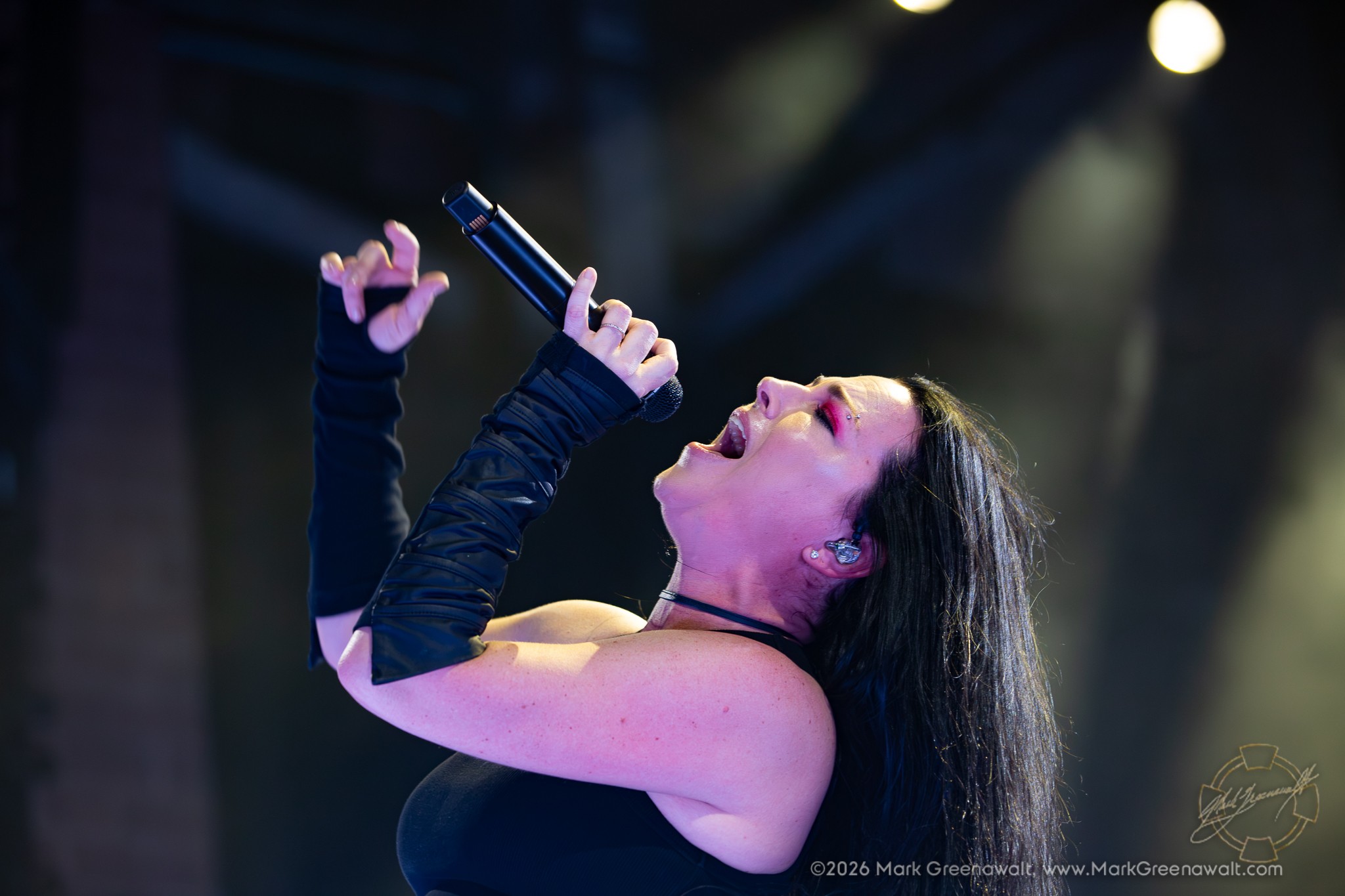 Amy Lee sings with her head tilted back, microphone raised above her mouth and one hand extended upward beneath soft white stage lights.