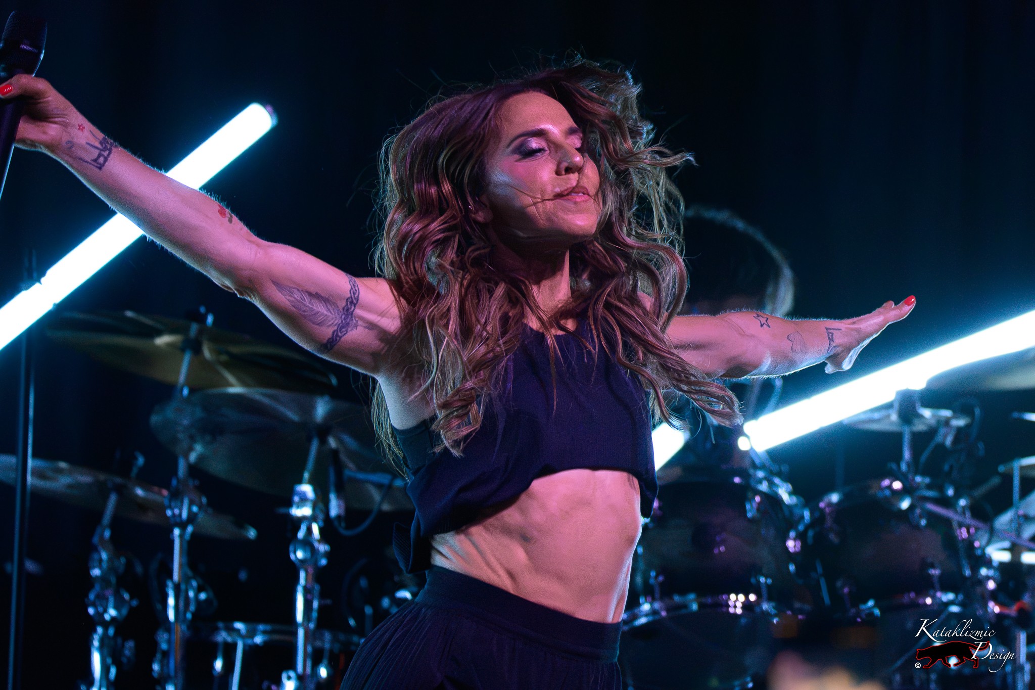Melanie C stretches both arms wide with her eyes closed under bright stage lights during The Melanie C World Tour in San Diego.