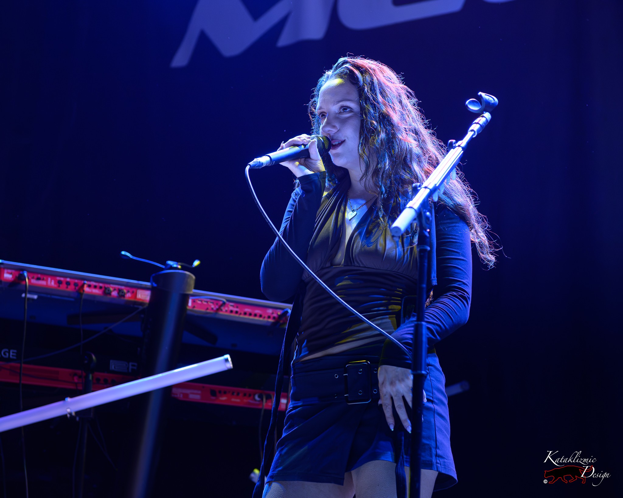 Sur Back sings into a microphone beneath deep blue stage lighting during her opening set at House of Blues San Diego.