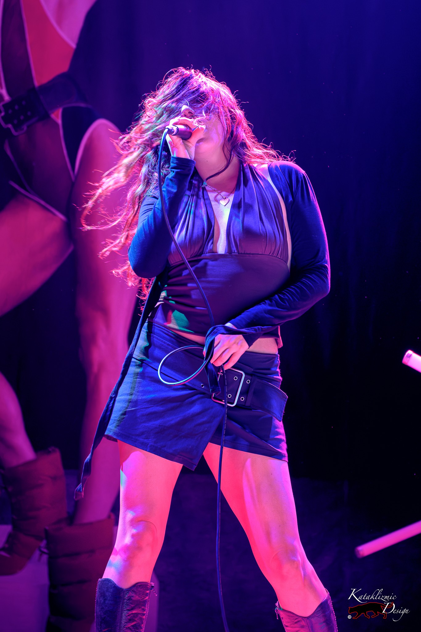 Sur Back sings into a microphone as her hair sweeps across her face under vivid pink and purple lighting at House of Blues San Diego.